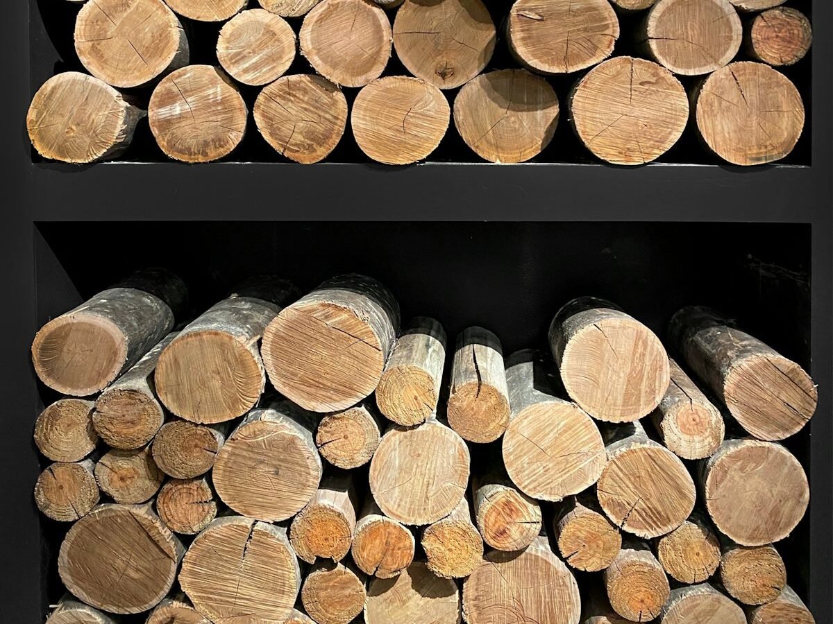 Rondins de bois clair rangés dans un meuble de rangement noir à deux niveaux