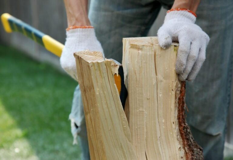 Mains gantées fendant une bûche de bois clair à la hache