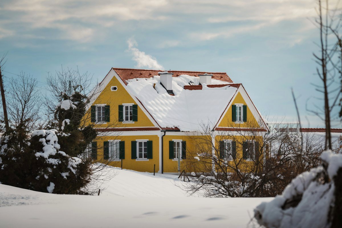 Maison jaune enneigée en hiver, avec de la fumée s'échappant de la cheminée